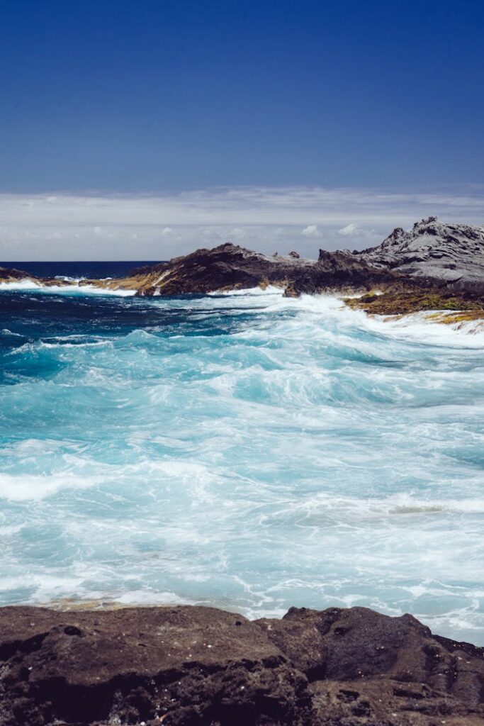 Gran Canaria Vibrant blue waves crashing against rugged rocks in Spain, under a clear blue sky.