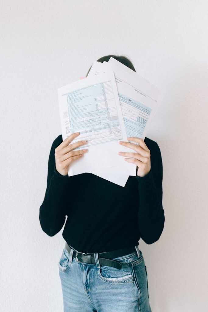 pexels photo 6919772 A woman concealing her face with tax forms, illustrating financial stress and paperwork burden.